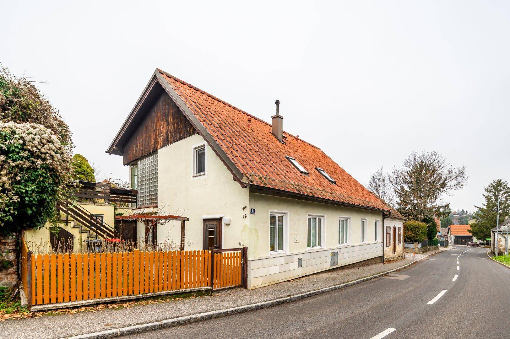 Ansicht des Hauses von der Straße mit Satteldach, Gaubenfenstern und einem Holzzaun im Vordergrund.