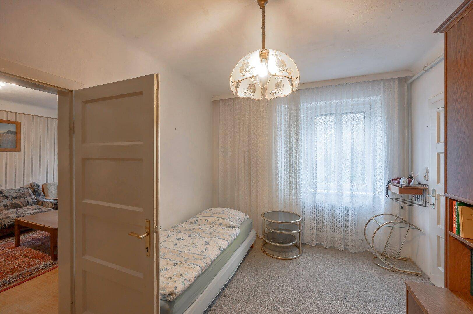 Kleines Schlafzimmer mit Einzelbett, Teppichboden und einem Fenster für natürliches Licht.
