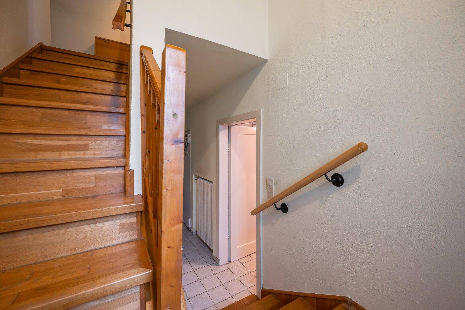 Holztreppe führt in die obere Etage, mit Fliesenboden im unteren Flurbereich.