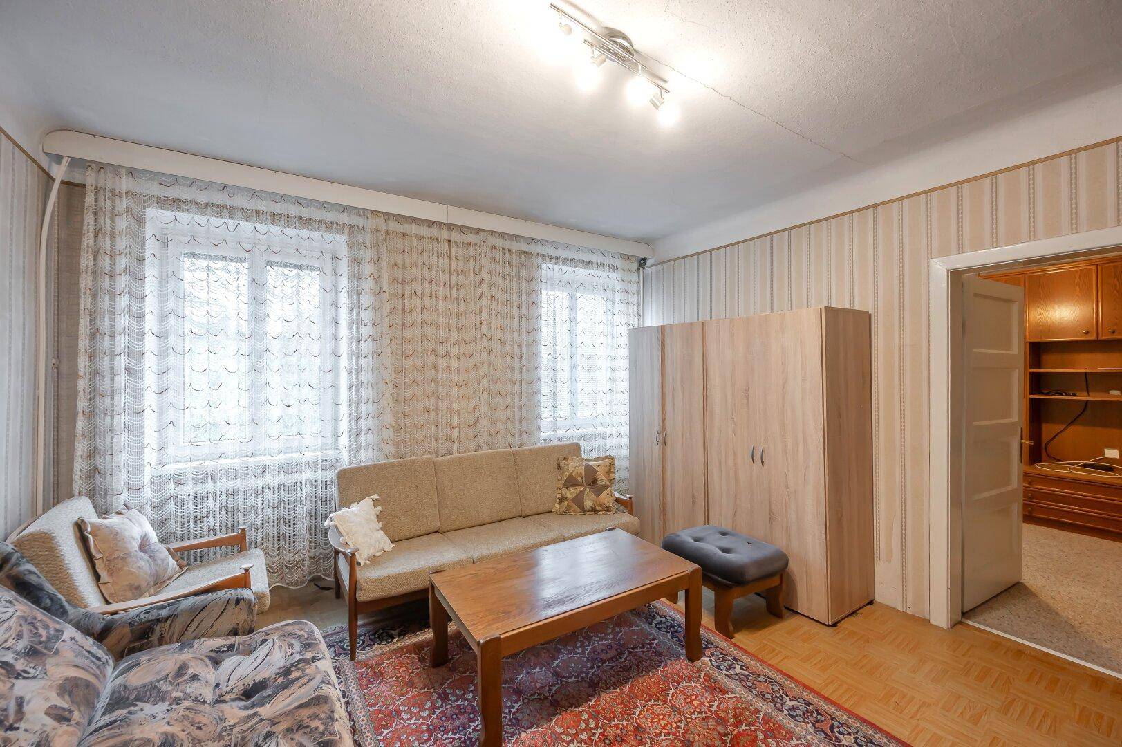 Gemütliches Wohnzimmer mit Sitzmöbeln, Couchtisch und Parkettboden, gut beleuchtet durch Fenster.