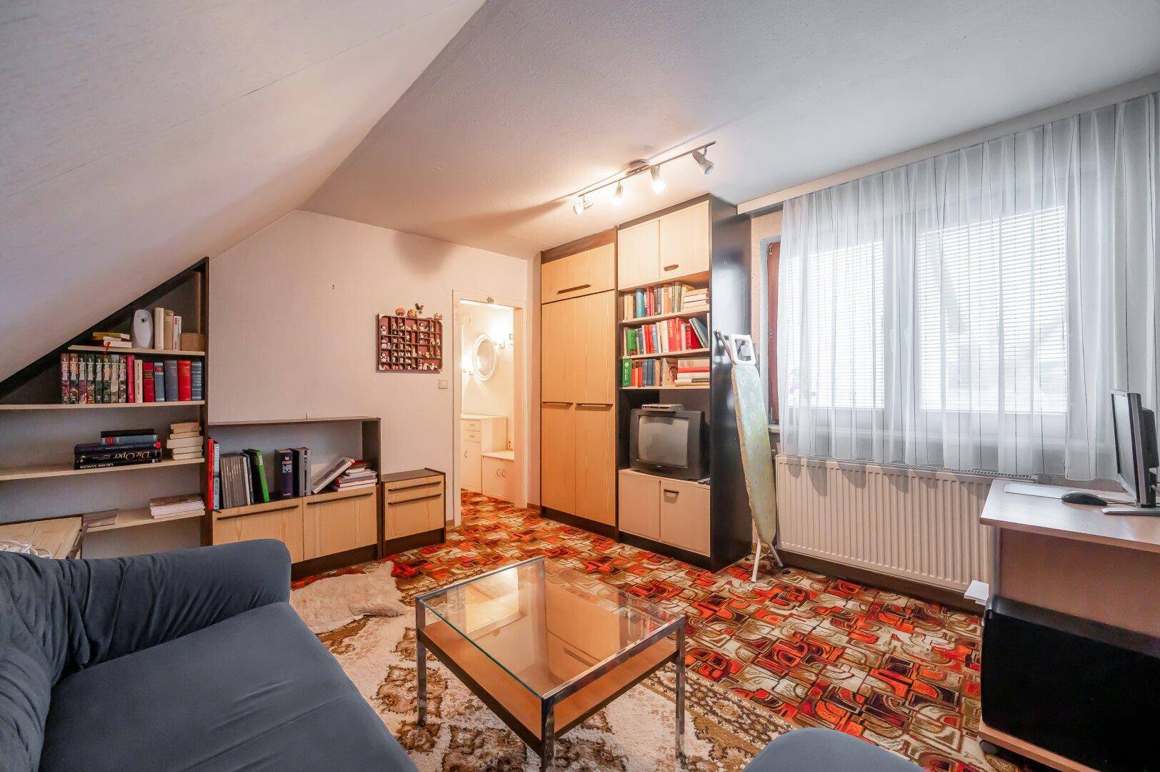 Wohnzimmer mit Sofa, Couchtisch und Wandschrank, ausgestattet mit gemustertem Teppichboden.