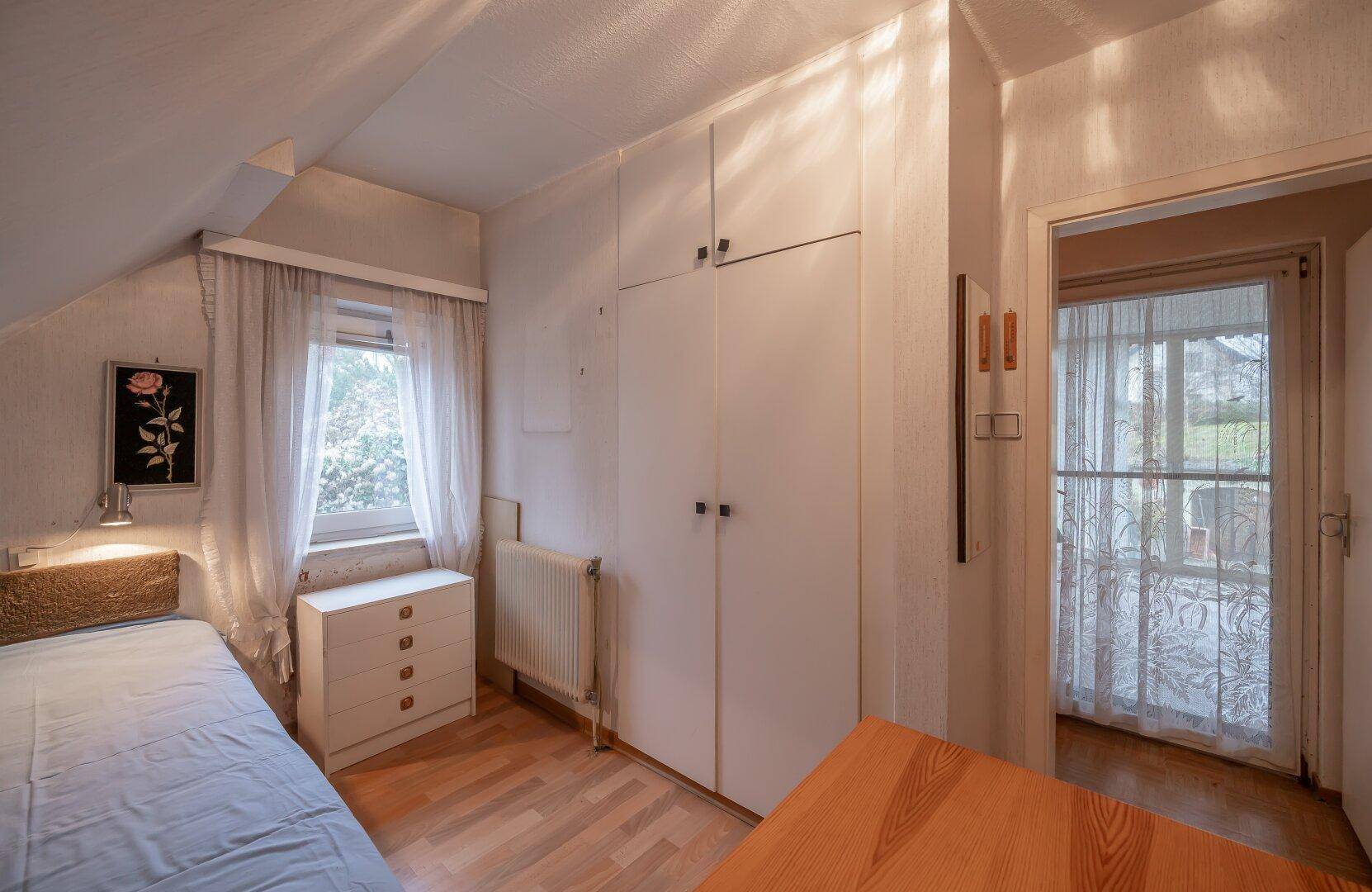 Schlafzimmer mit Einzelbett, Kleiderschrank und Holzboden, mit Zugang zum Wintergarten.