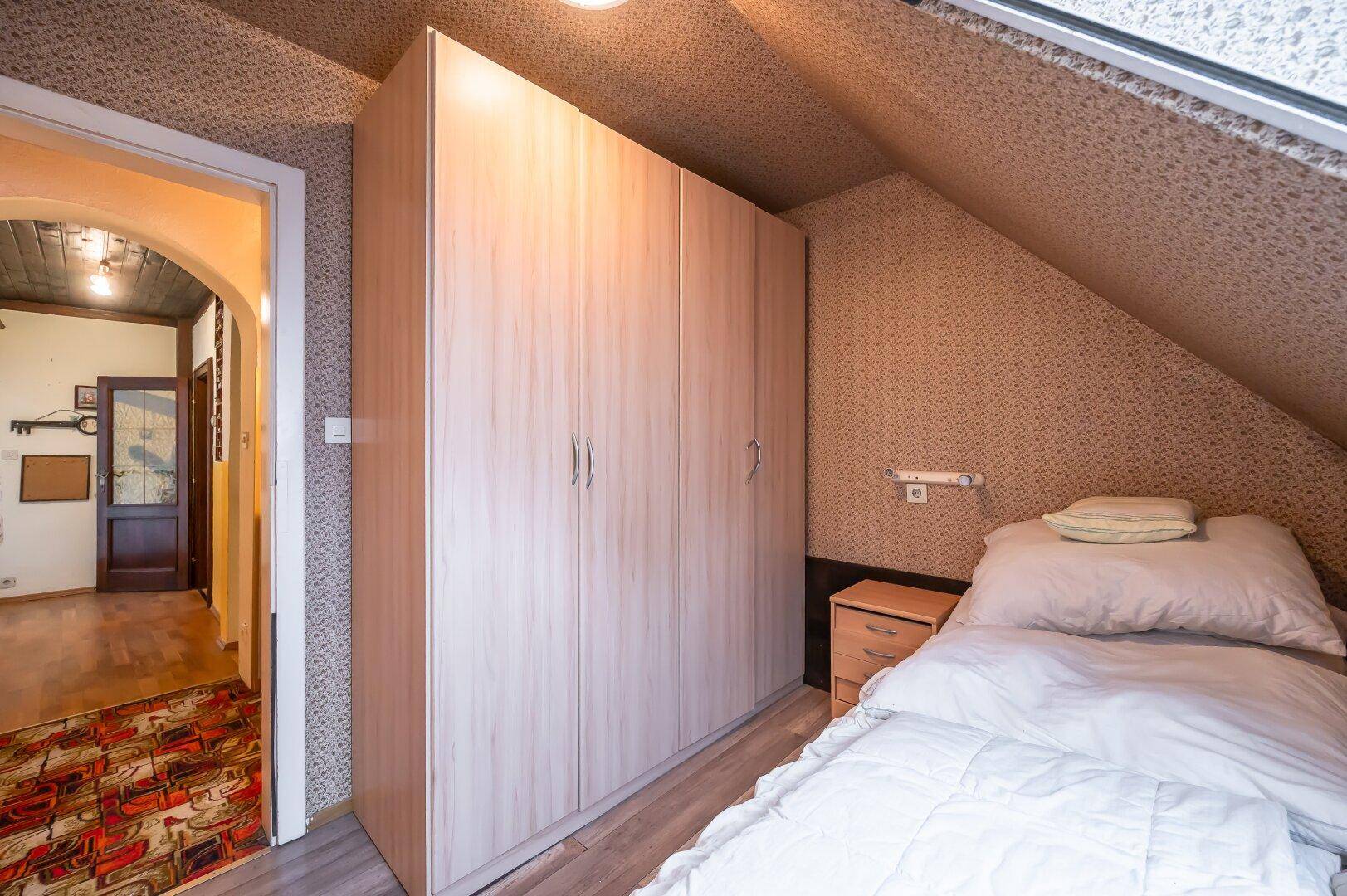 Schlafzimmer mit Einzelbett, großem Kleiderschrank und Dachschräge, gemütlich eingerichtet.