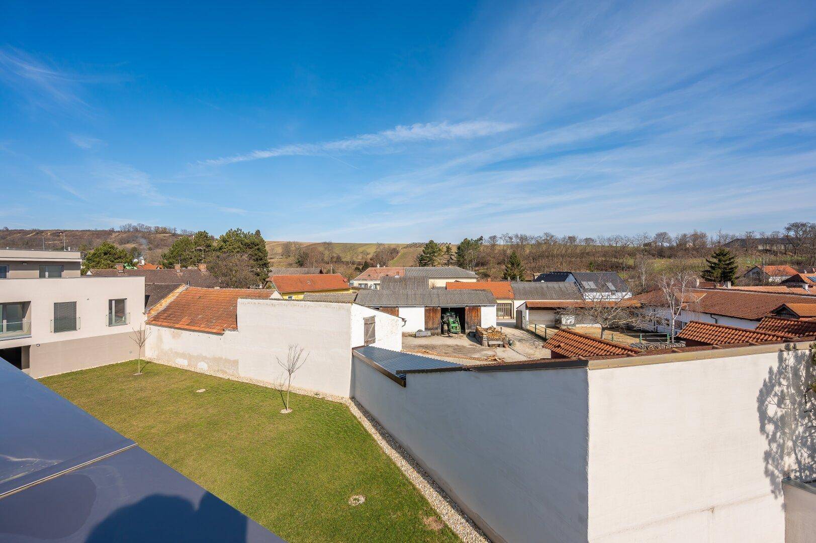 Blick auf einen grünen Gartenbereich und die umliegende ländliche Bebauung.