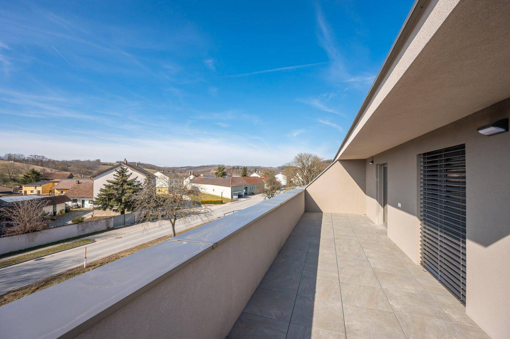 Langer Balkon mit Fliesenboden und Blick auf die Straße und die umliegende Landschaft.