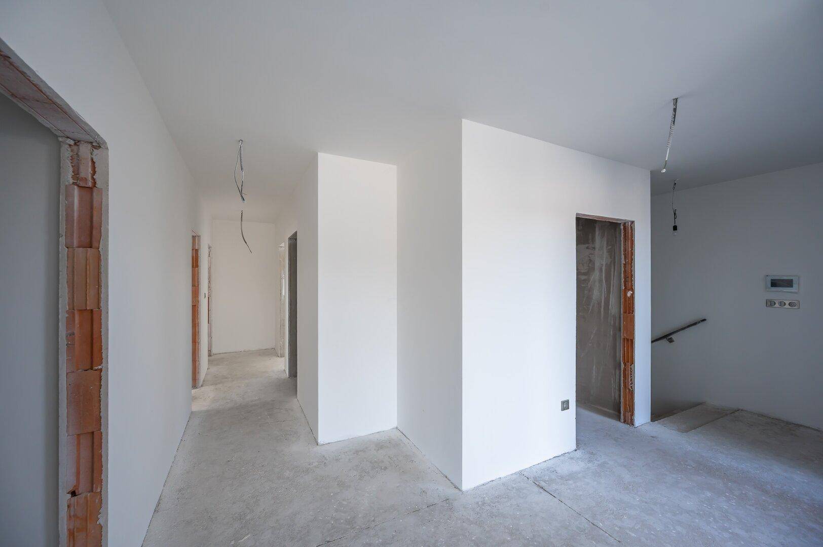 Unfertiger Innenraum mit weißen Wänden und Betonboden, bereit für den Ausbau.