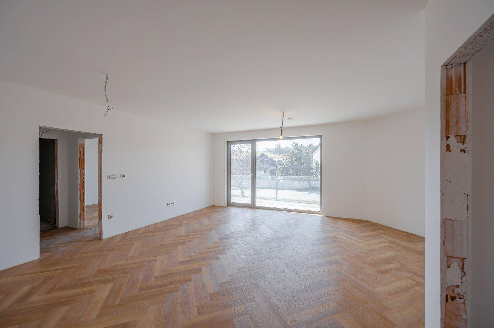 Geräumiges, helles Zimmer mit Fischgrätparkett und großer Fensterfront mit Blick ins Grüne.