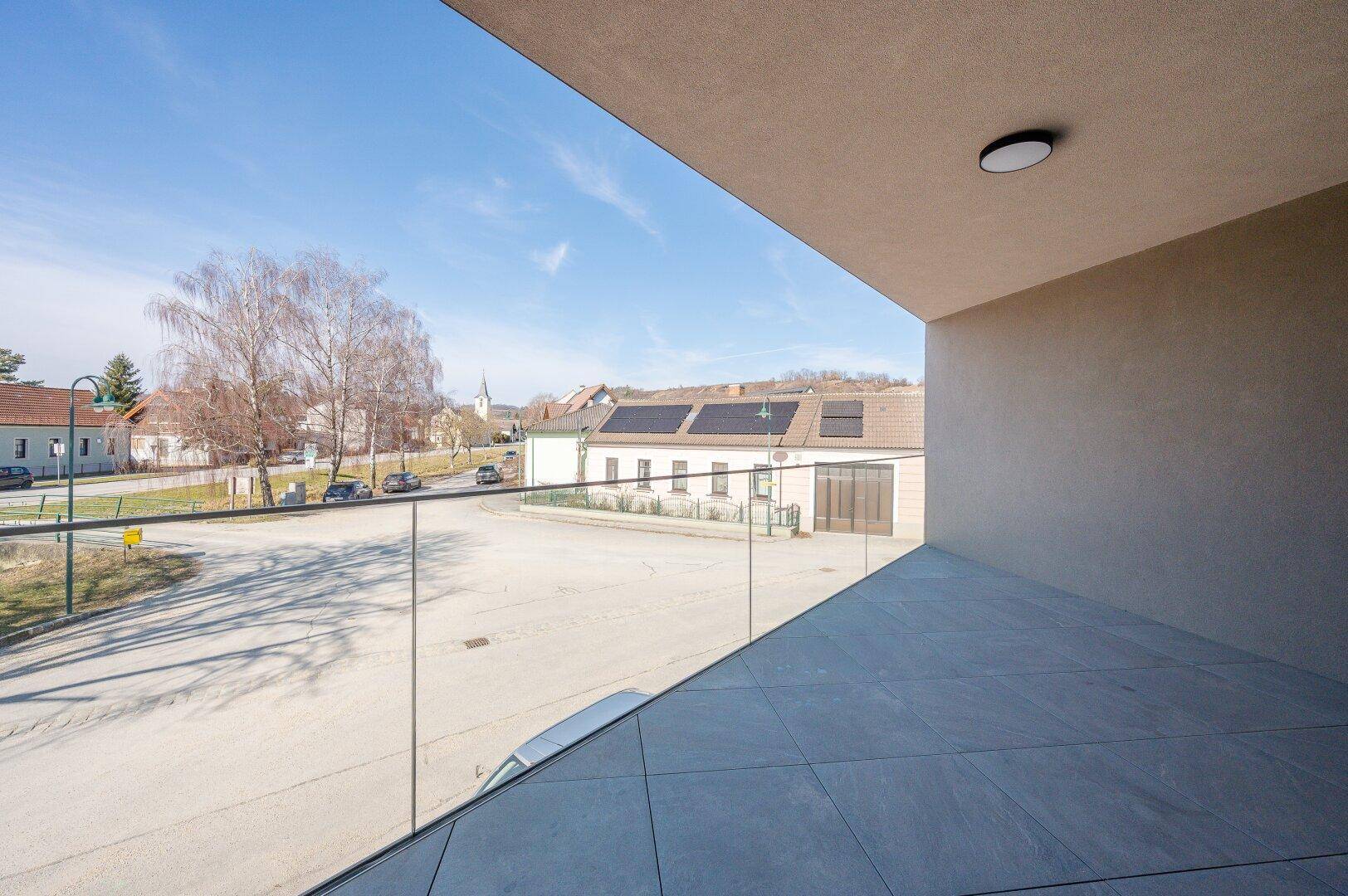 Sonniger Terrassenbereich mit modernem Glasgeländer und Weitblick über die Umgebung.