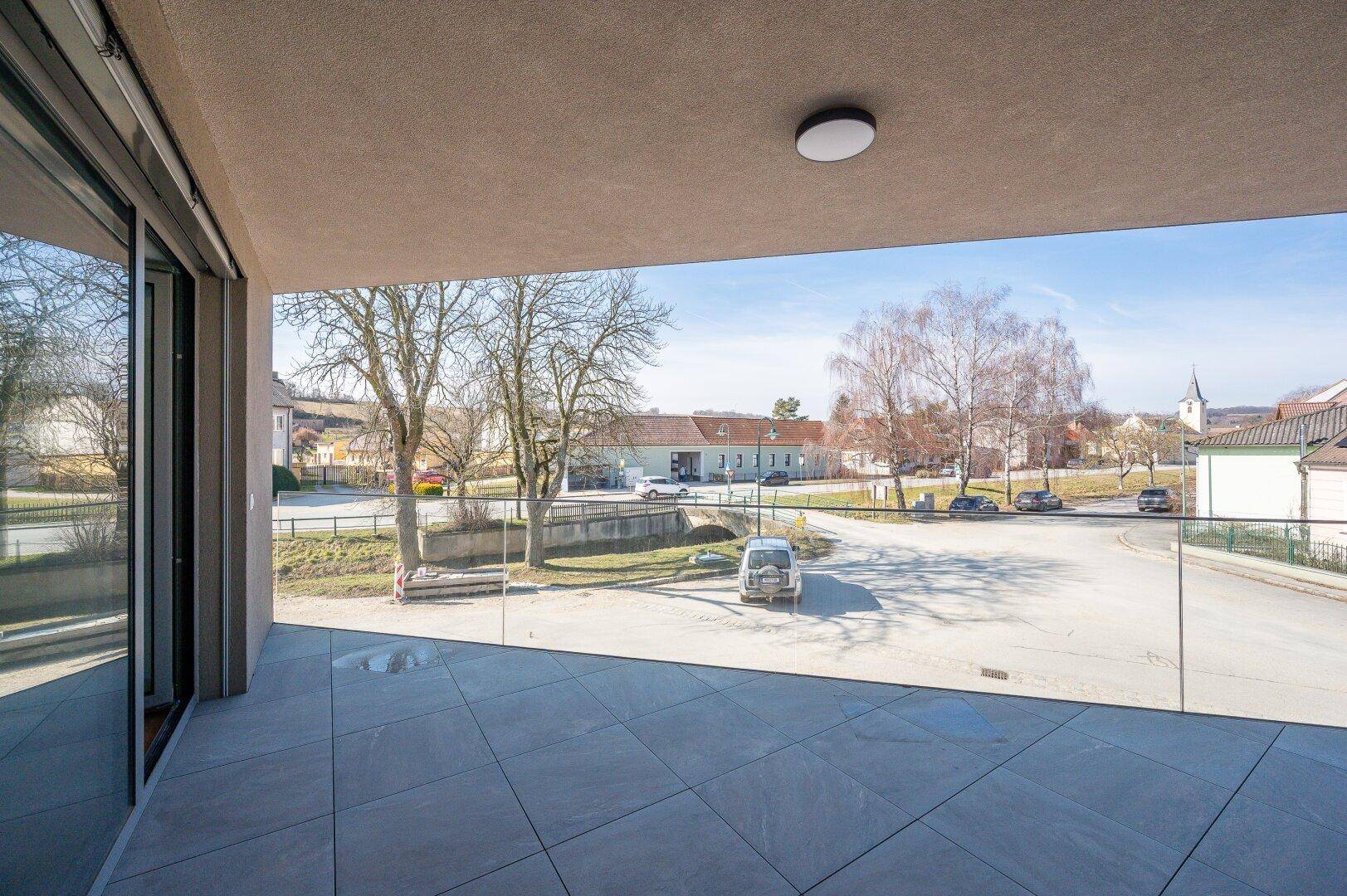 Geräumige Terrasse mit Glasgeländer und Blick auf die umliegende Nachbarschaft und Straße.