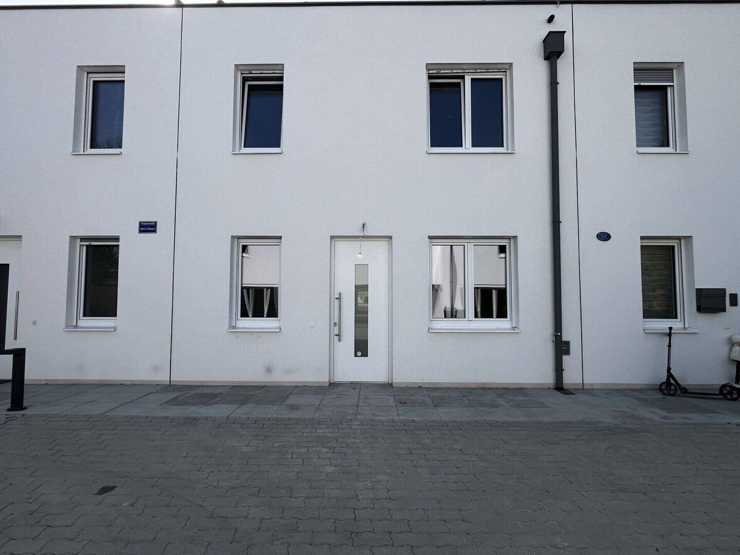 Moderne weiße Reihenhausfassade mit mehreren Fenstern und Eingangstür.