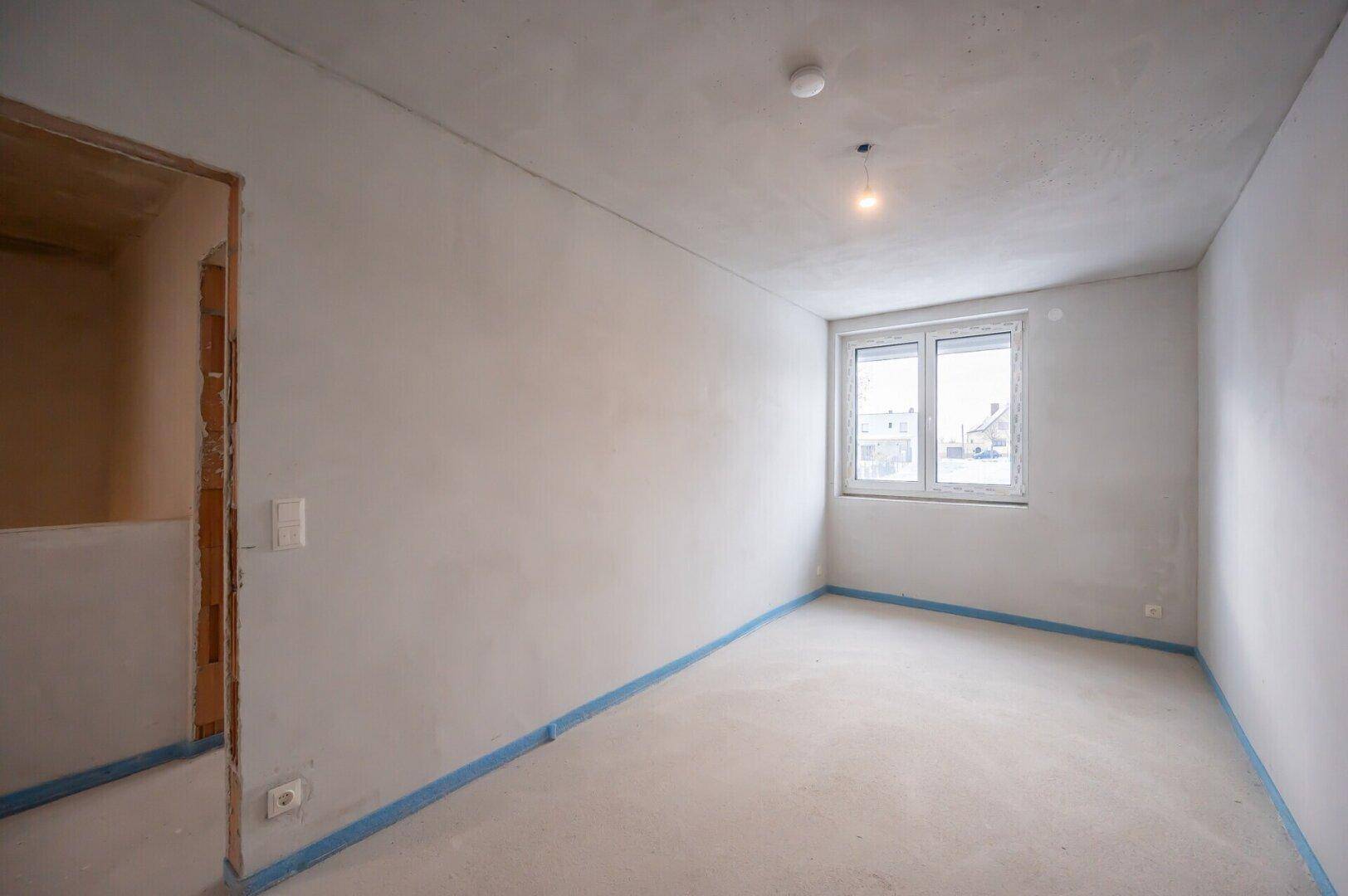 Schlafzimmer im Rohbau mit einem Fenster und unfertigen Wänden.