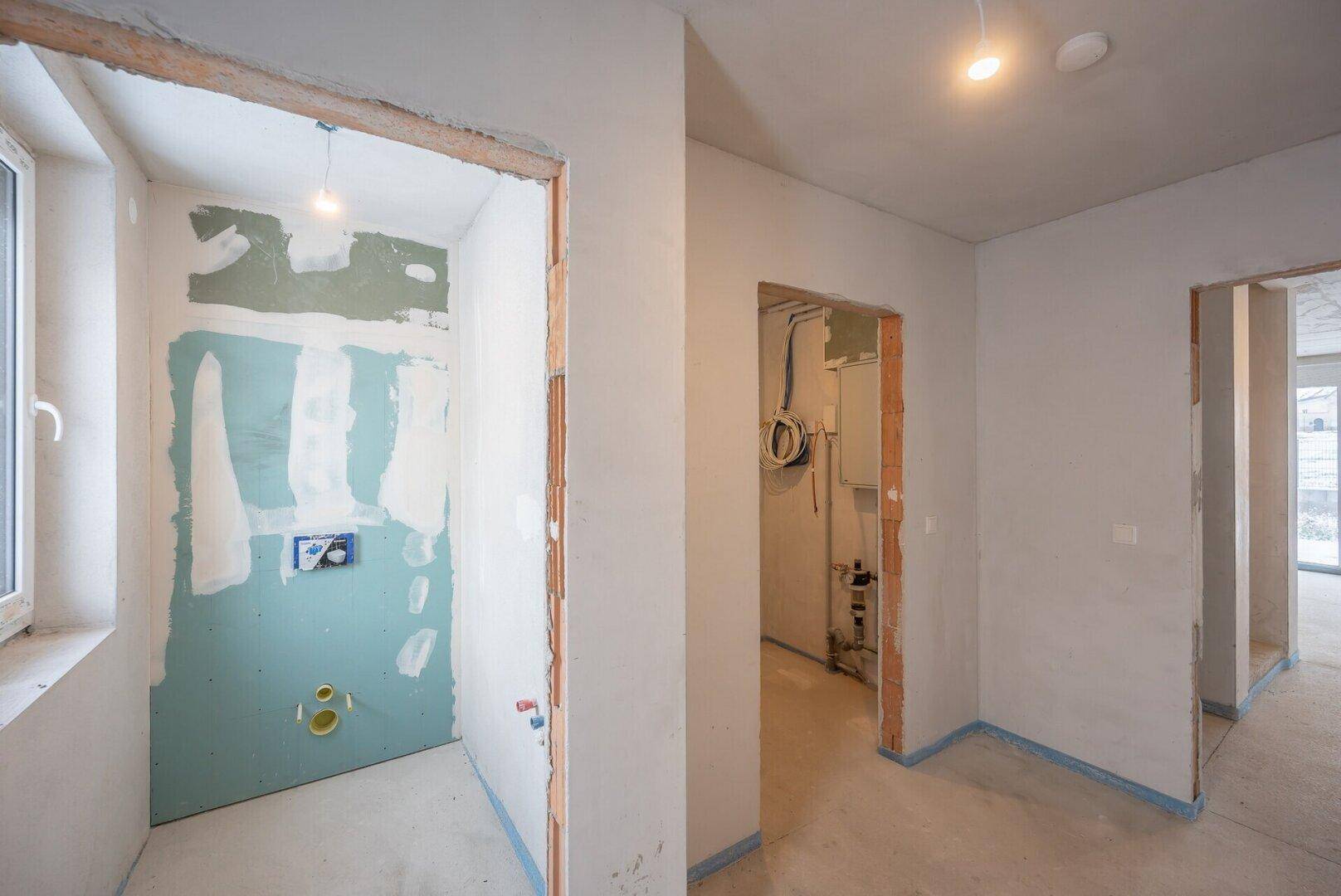 Badezimmer im Rohbau mit vorbereiteten Anschlüssen und Fenster für Tageslicht.