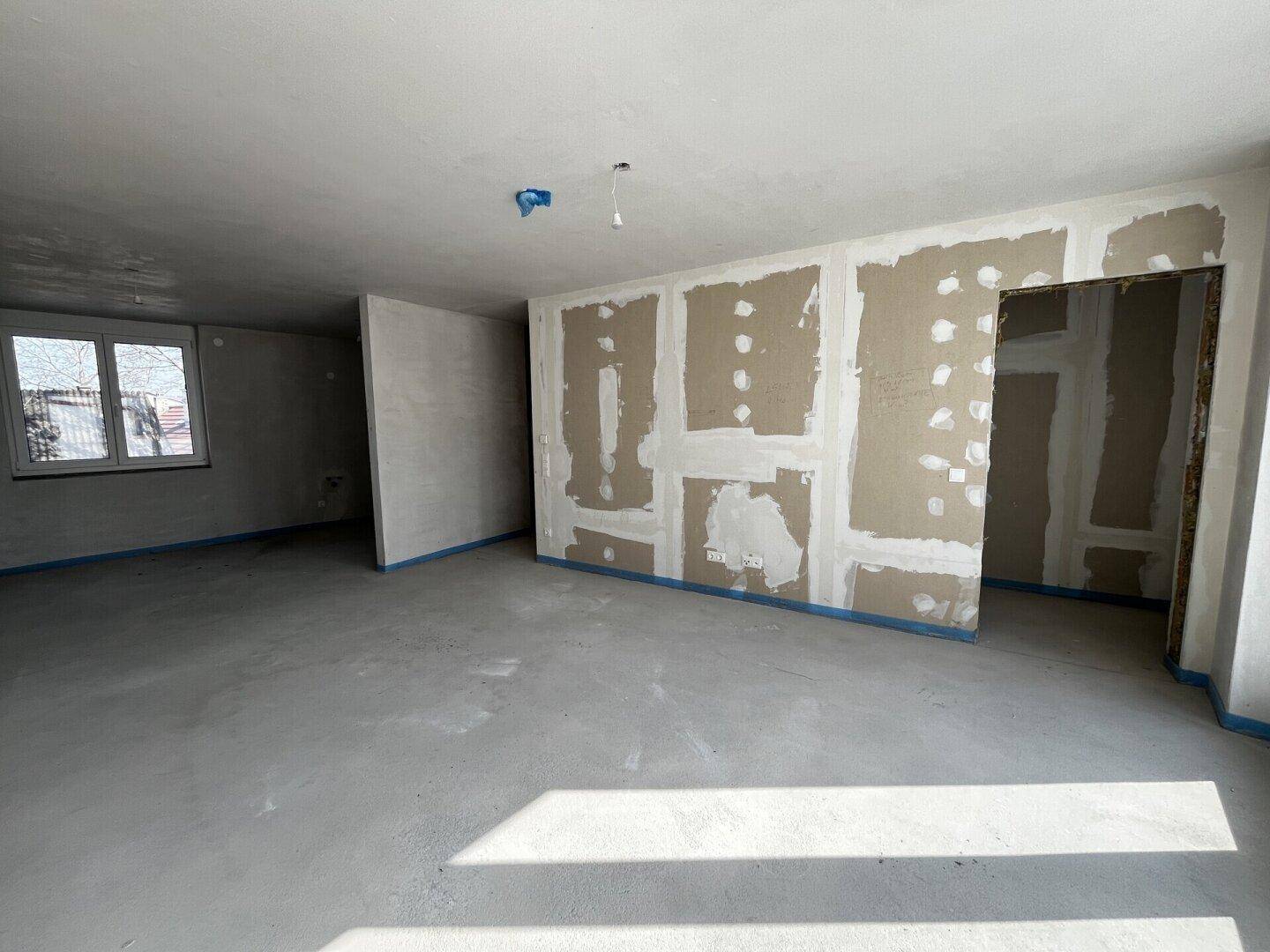 Geräumiger Raum im Rohbau mit vorbereiteten Wänden und Betonboden.