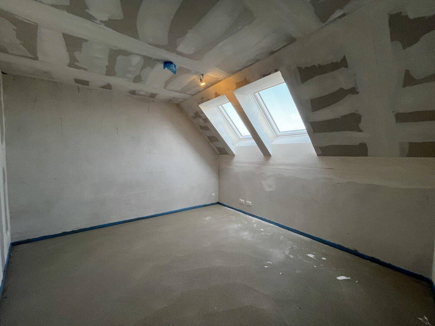Raum im Rohbau mit Dachschrägen und zwei Dachfenstern für viel Licht.