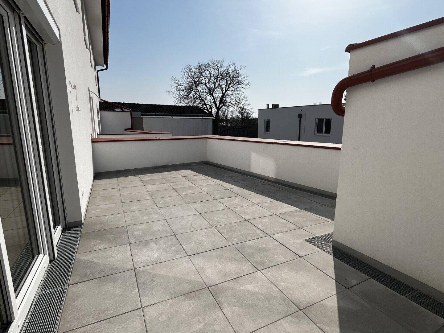 Große, leere Terrasse mit Fliesenboden und Blick auf die Umgebung.