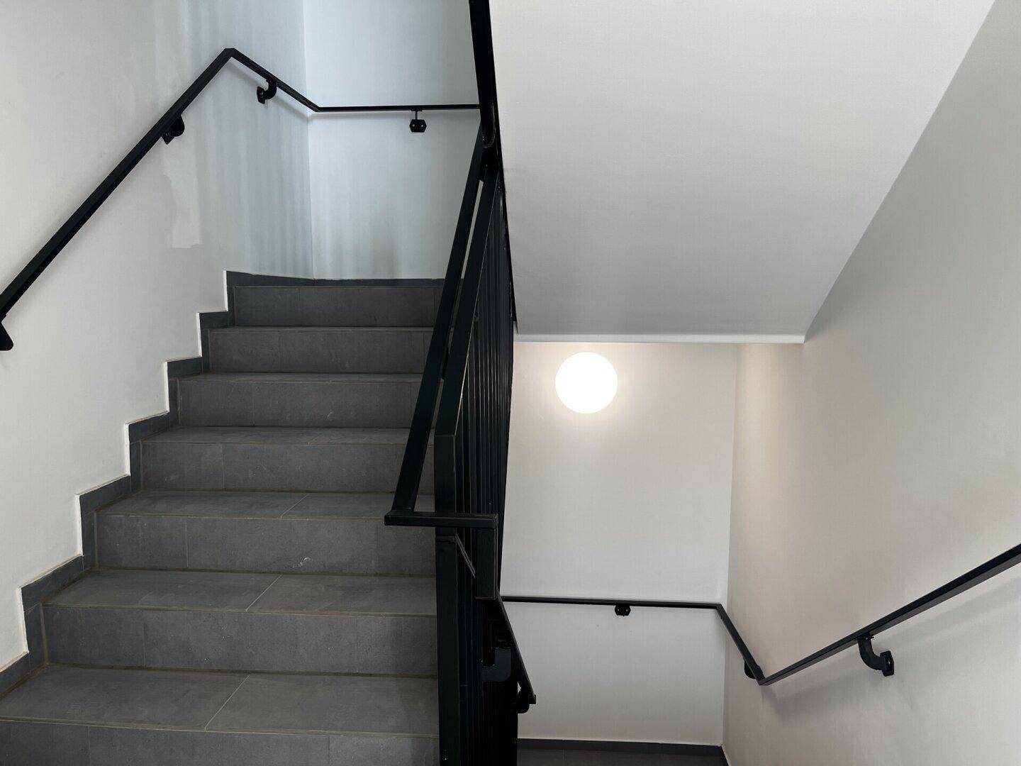 Modernes Treppenhaus mit grauen Fliesenstufen und schwarzem Geländer.