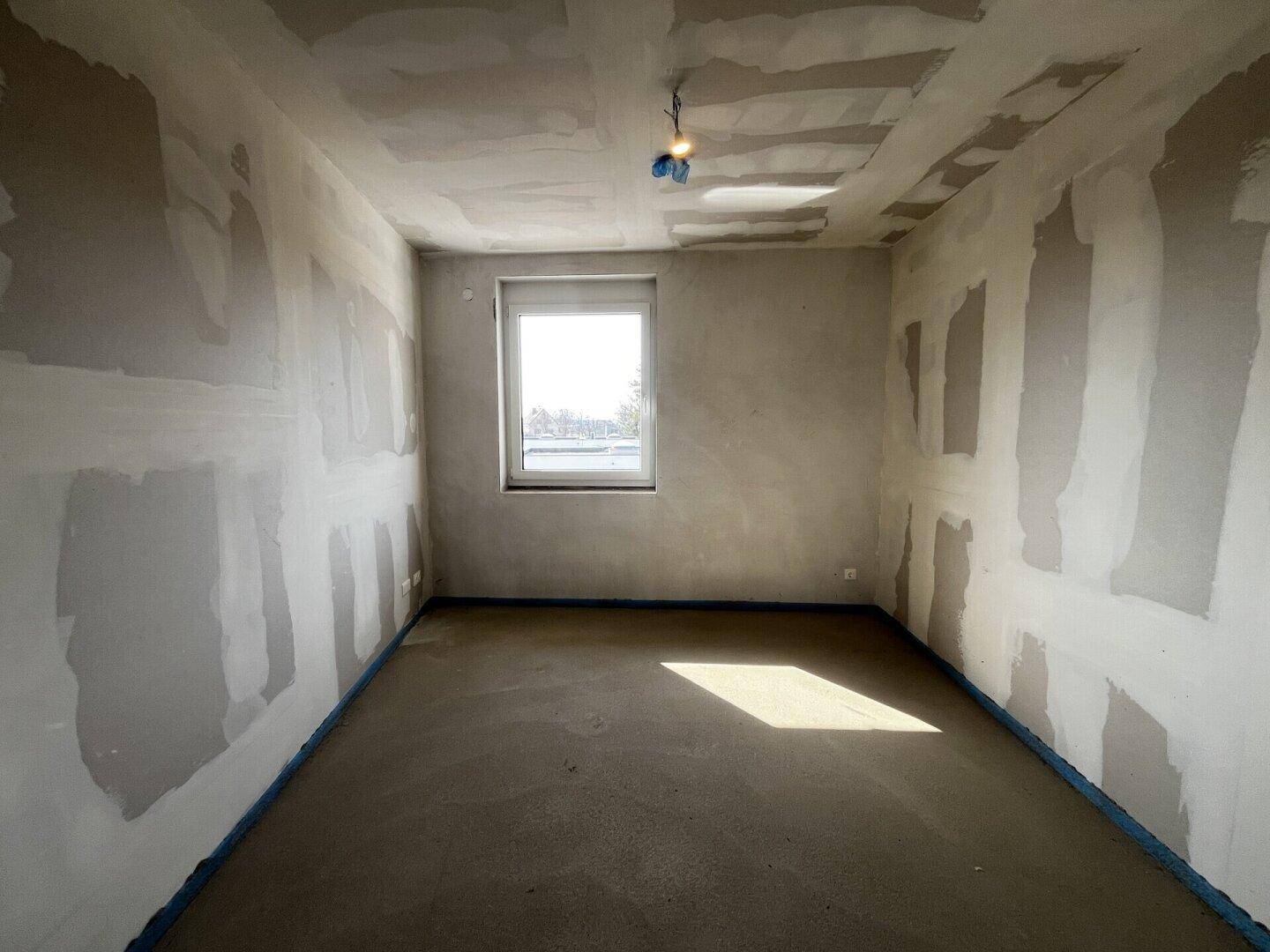 Unfertiger Raum mit Fenster, Betonboden und vorbereiteten Wänden.