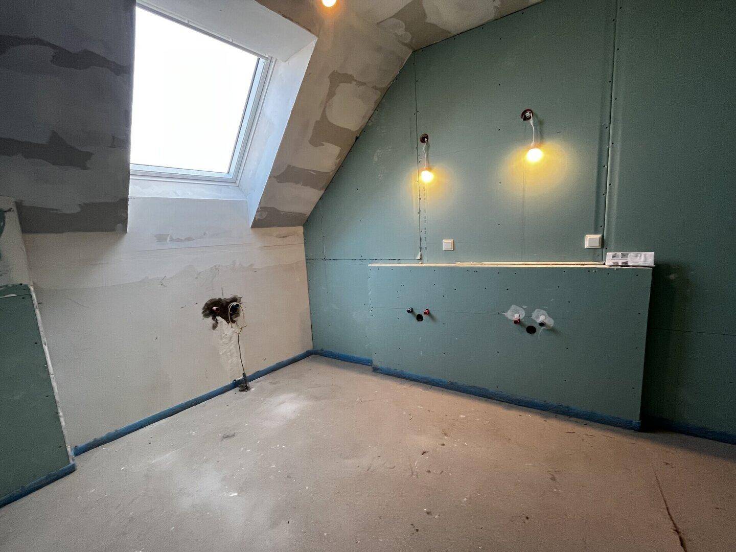Badezimmer im Rohbau mit Dachschräge, Dachfenster und vorbereiteten Installationen.