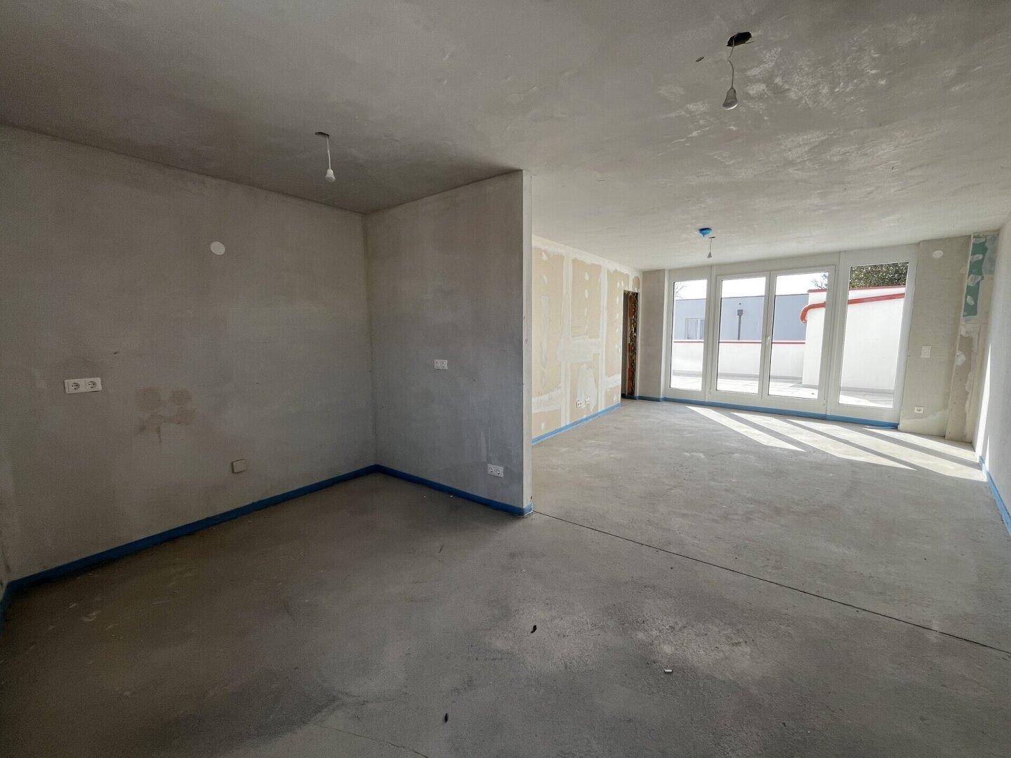Großer Raum im Rohbau mit Zugang zu einer Terrasse und viel Tageslicht.