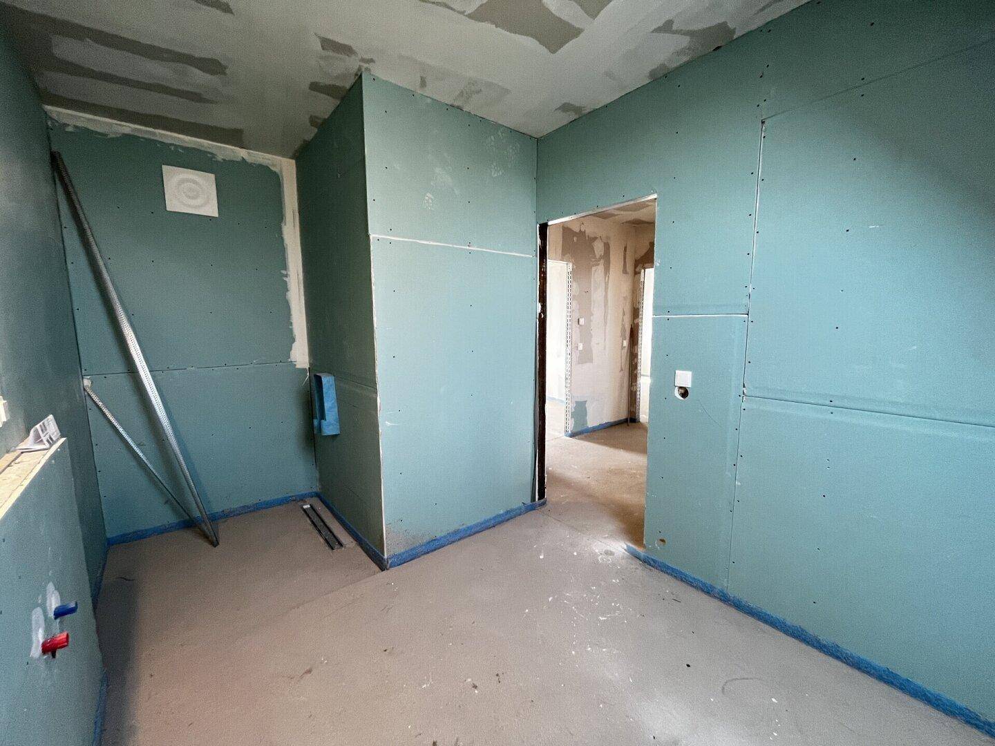 Badezimmer im Rohbau mit vorbereiteter Duschfläche und Installationen.