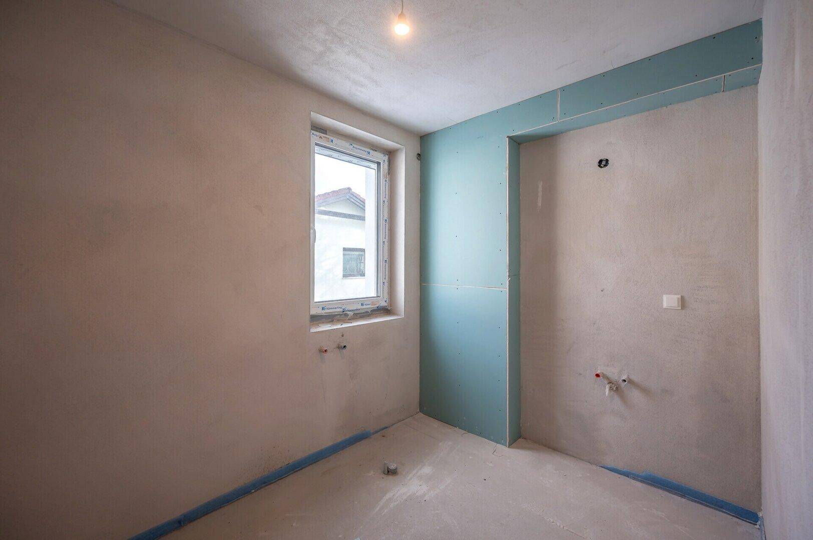 Rohbau-Badezimmer mit Fenster und vorbereiteten Wänden für die Installation von Sanitärobjekten.
