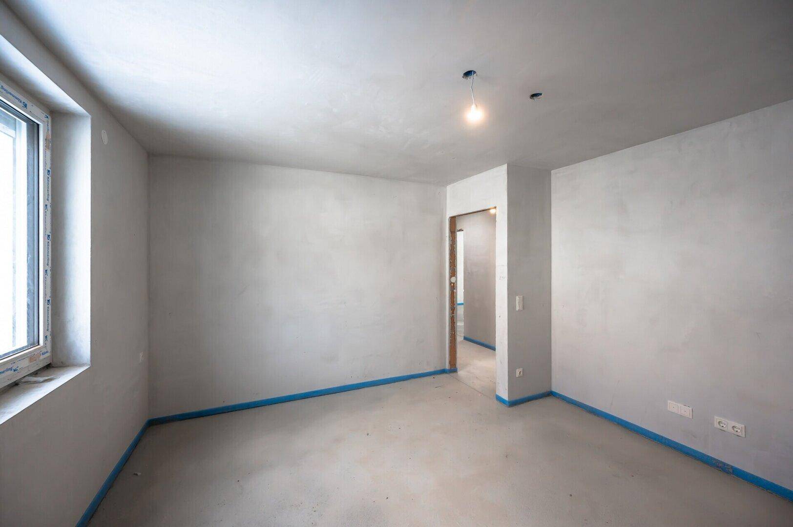 Rohbau-Raum mit Fenster und offener Tür zu einem weiteren Bereich, ideal für individuelle Gestaltung.