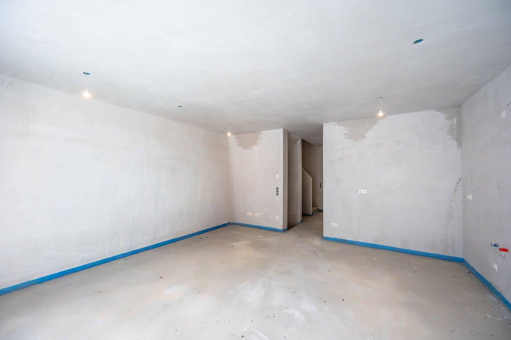Geräumiger Rohbau-Raum mit Betonboden und unverputzten Wänden, bereit für den Innenausbau.