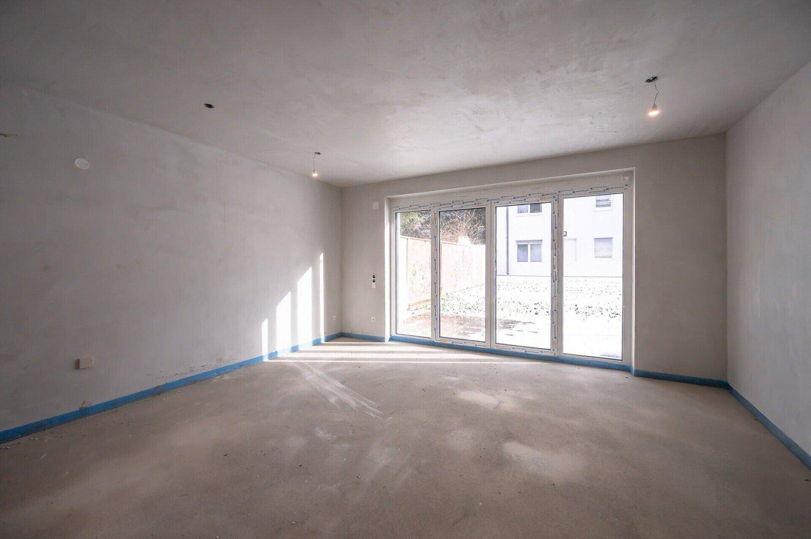 Heller Rohbau-Raum mit großer Fensterfront und viel natürlichem Licht, bereit für den Ausbau.