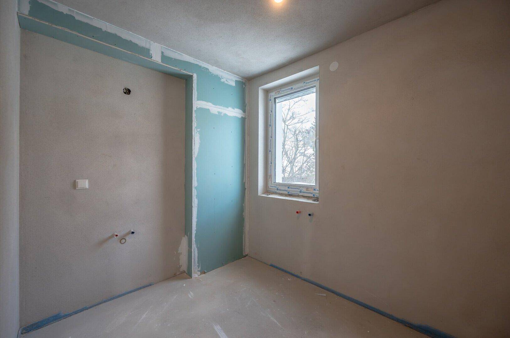 Unfertiger Raum im Rohbau mit Fenster und blauer Abdichtung, bereit für den weiteren Ausbau.