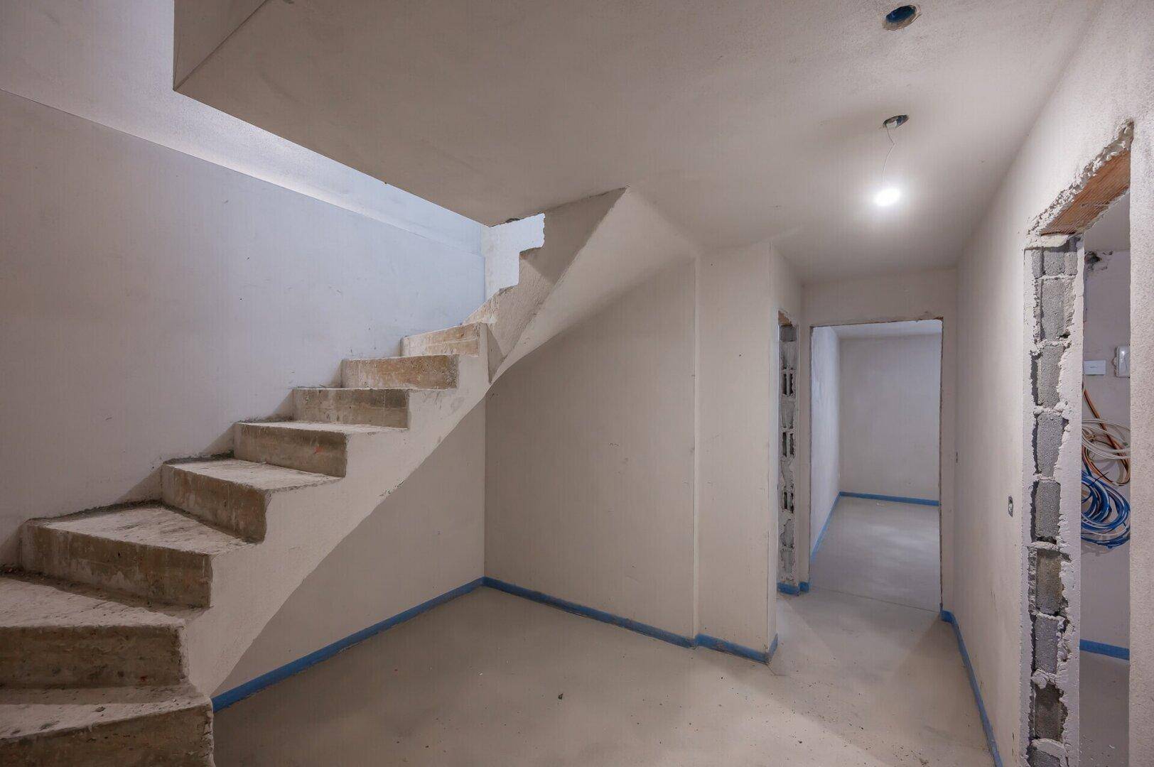 Unfertiger Treppenbereich im Rohbau mit rohen Betonstufen und angrenzendem Flur.
