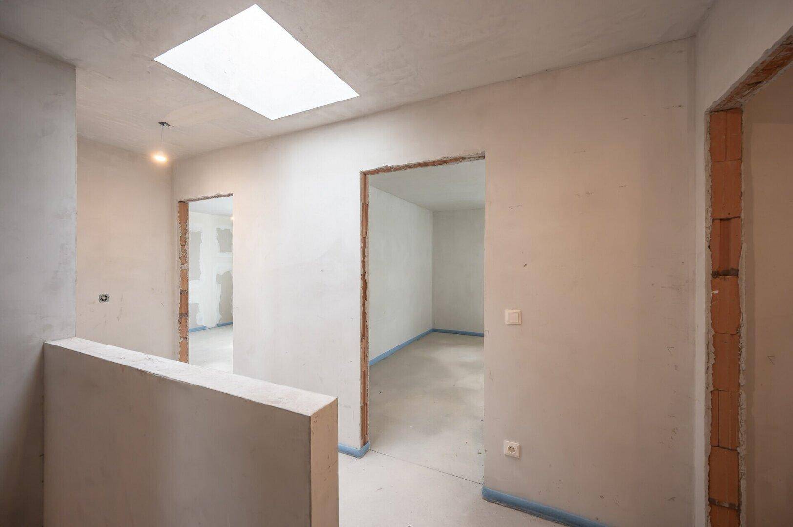 Heller Flur im Rohbau mit mehreren Türöffnungen und einem Oberlicht für Tageslicht.