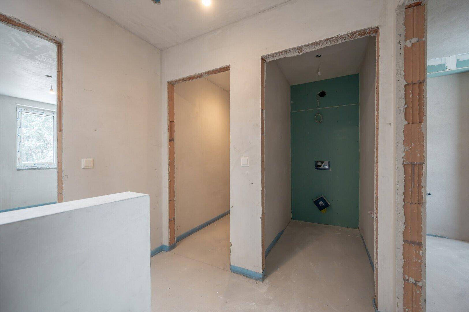Unfertiger Flur im Rohbau mit zwei Türöffnungen, eine davon mit blauer Abdichtung.