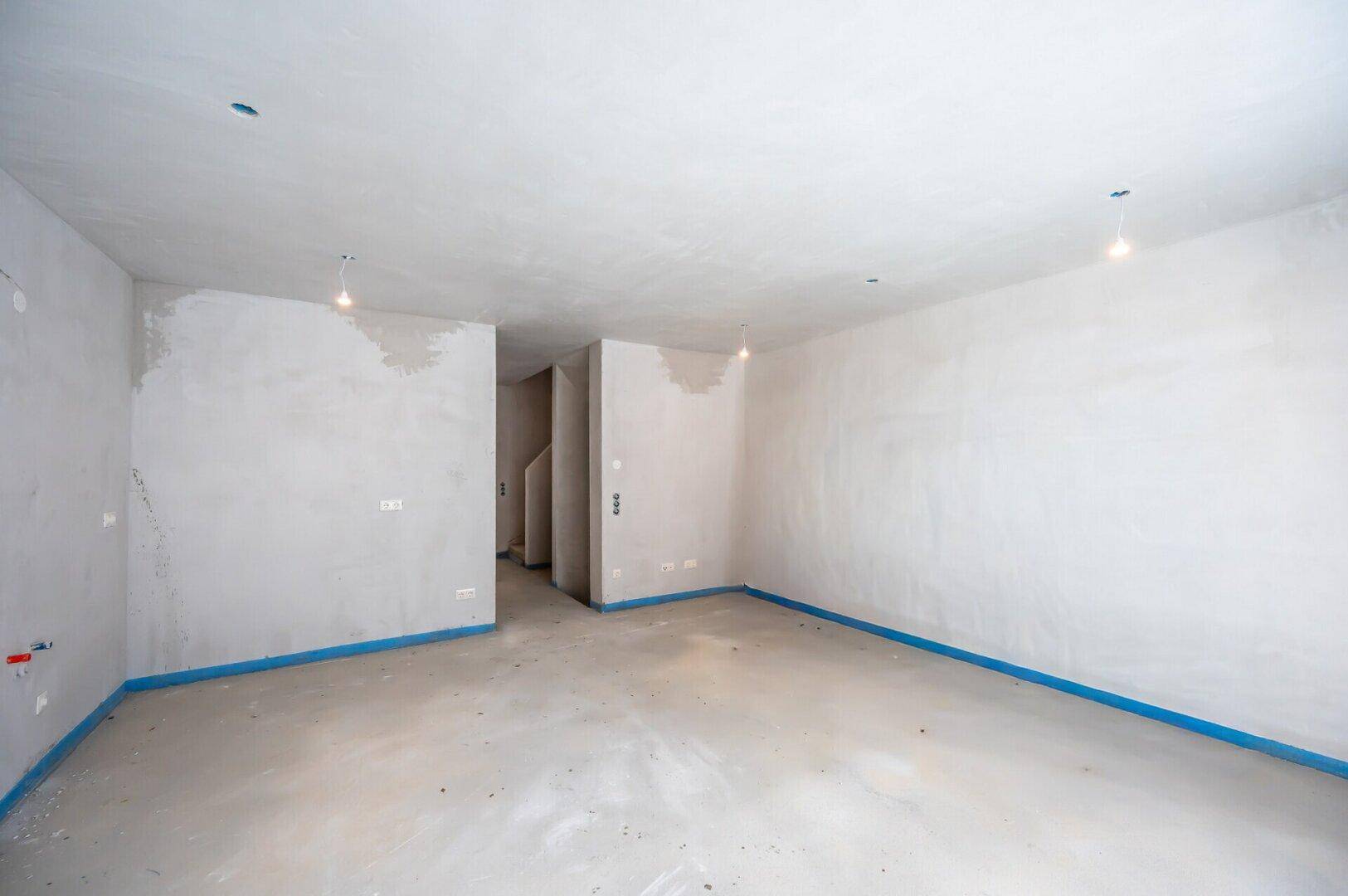 Großer, leerer Raum im Rohbau mit Betonboden und weißen Wänden, bereit für den Ausbau.