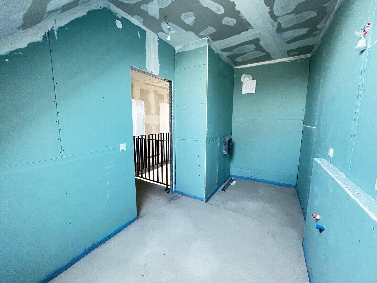 Rohbau-Badezimmer mit grünen Trockenbauwänden und sichtbaren Installationen für Sanitäranlagen.