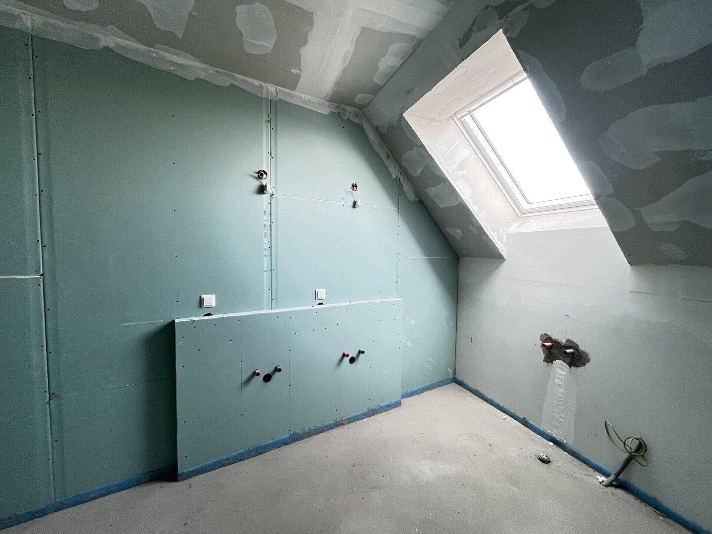 Rohbau-Badezimmer im Dachgeschoss mit schräger Decke, Dachfenster und sichtbaren Sanitärinstallationen.