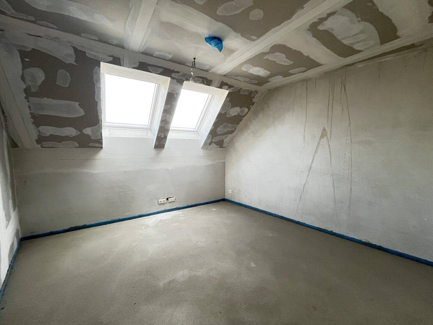 Helles Rohbau-Schlafzimmer im Dachgeschoss mit zwei großen Dachfenstern, die viel Licht spenden.