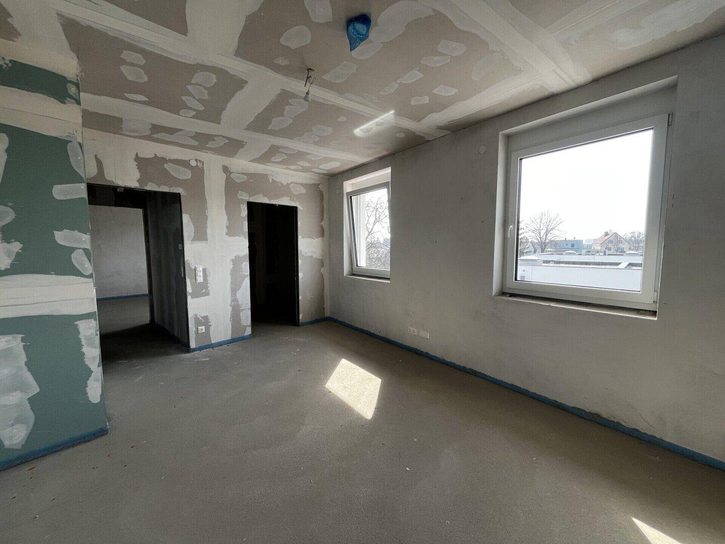 Unfertiges Zimmer mit zwei Fenstern und Betonboden, bereit für die individuelle Gestaltung.