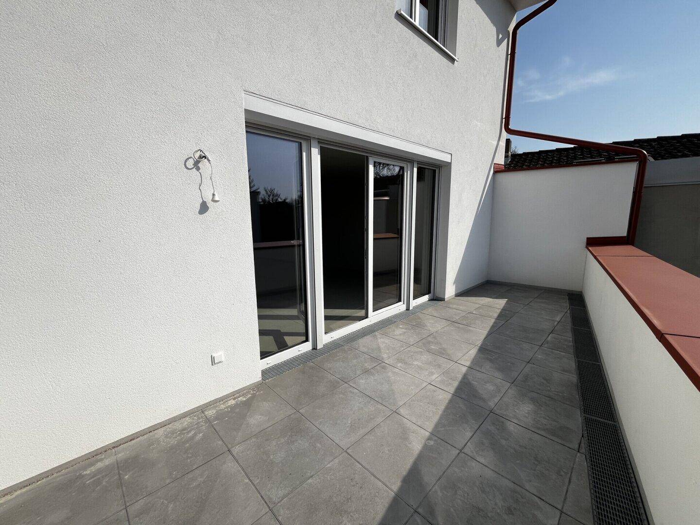 Sonniger Terrassenbereich mit großen Glasschiebetüren, die den Zugang zum Innenraum ermöglichen.