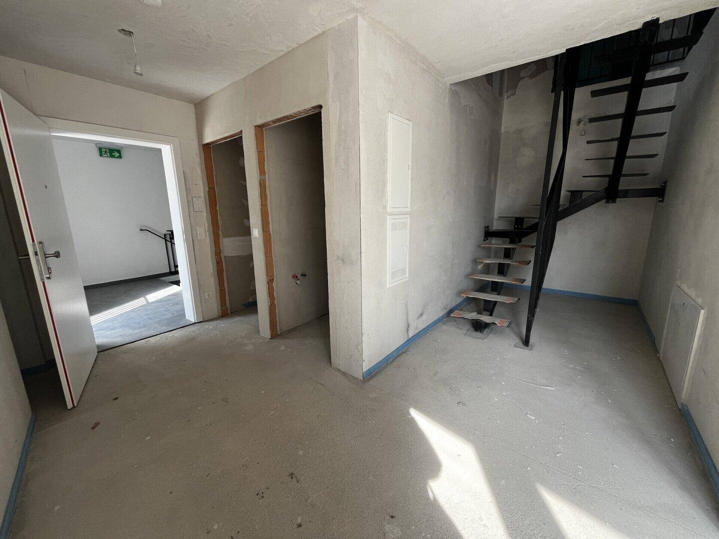 Rohbau-Flur mit offener Treppe und Betonboden, der auf den weiteren Ausbau wartet.