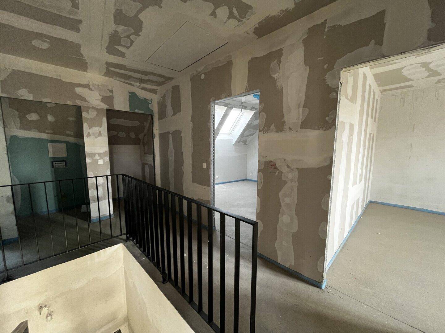 Rohbau-Dachgeschoss mit Treppengeländer und vorbereiteten Räumen, inklusive Dachfenster für natürliches Licht.