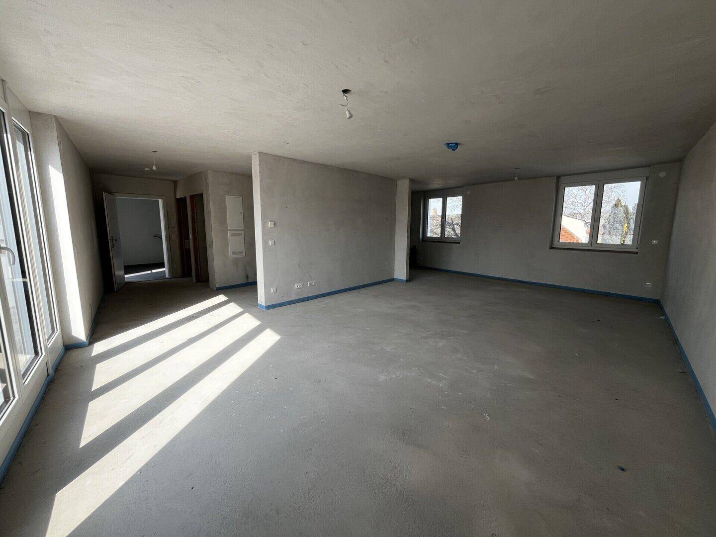Heller Rohbau-Wohnbereich mit Betonboden und mehreren Fenstern, bereit für den Innenausbau.