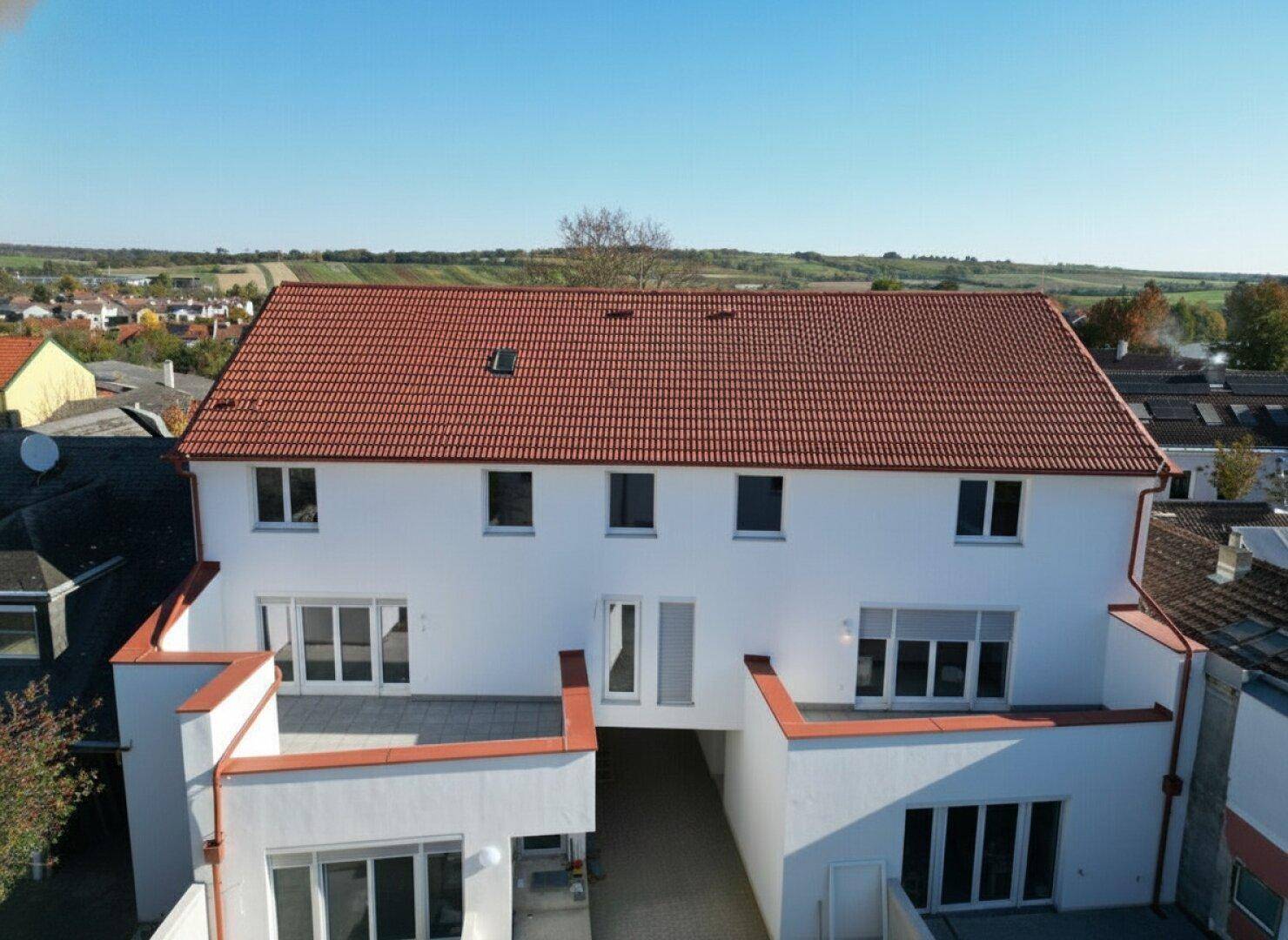 Neubau mit rotem Ziegeldach und weißer Fassade, umgeben von ländlicher Landschaft.