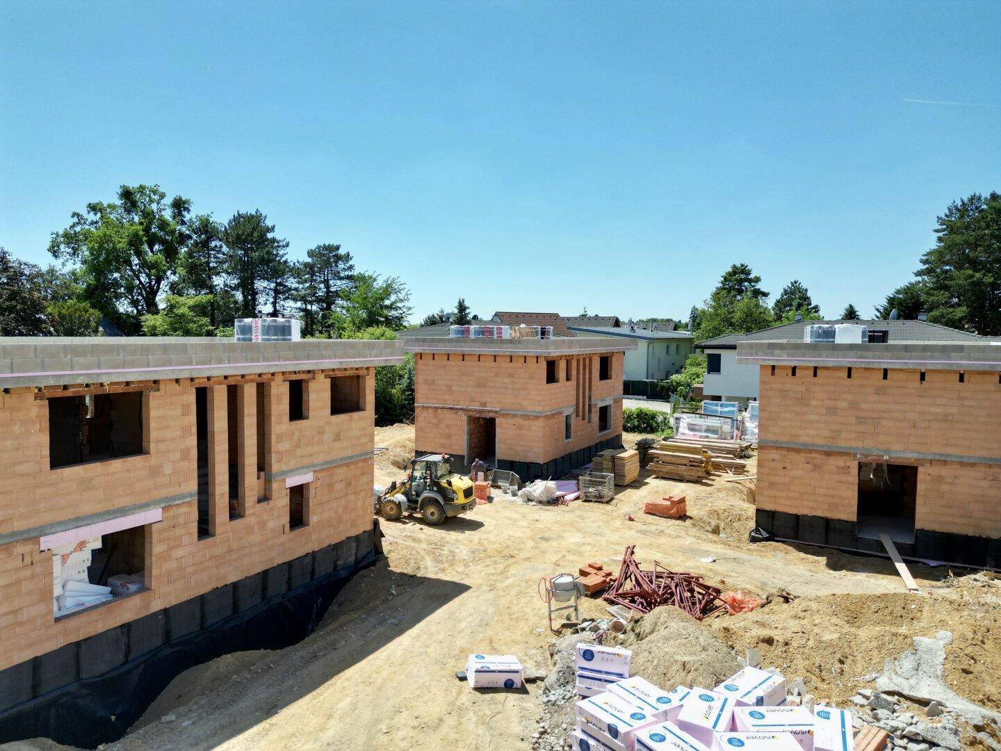 Baustelle mit mehreren im Bau befindlichen Häusern unter blauem Himmel und viel Erde.