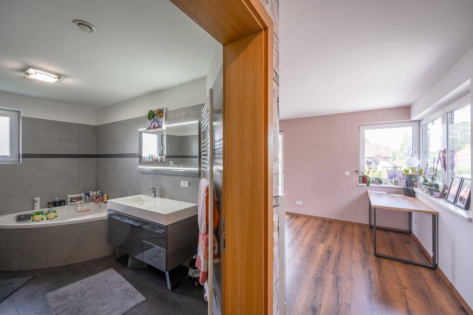 Modernes Badezimmer mit Eckbadewanne, Waschtisch und Zugang zu einem hellen Zimmer.