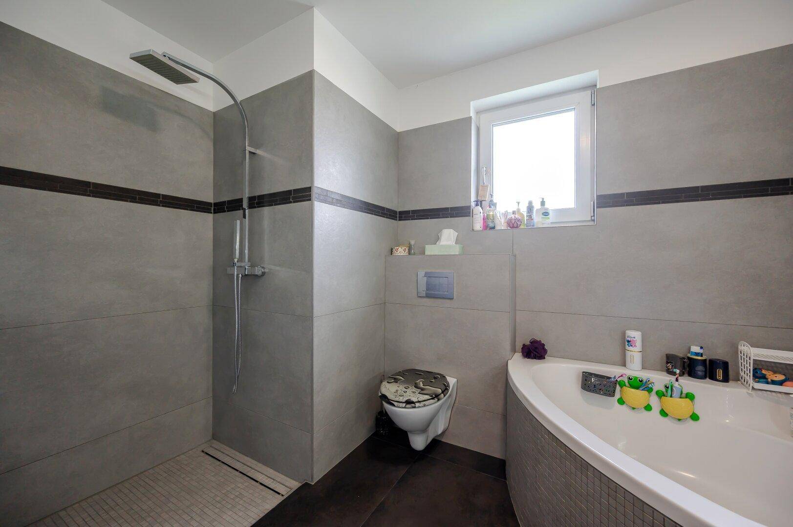 Modernes Badezimmer mit großer Dusche, Eckbadewanne und Wand-WC, hell gefliest.
