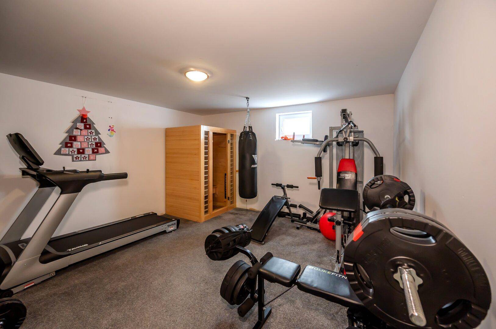 Geräumiger Fitnessraum im Untergeschoss mit verschiedenen Trainingsgeräten und einer Infrarotsauna.