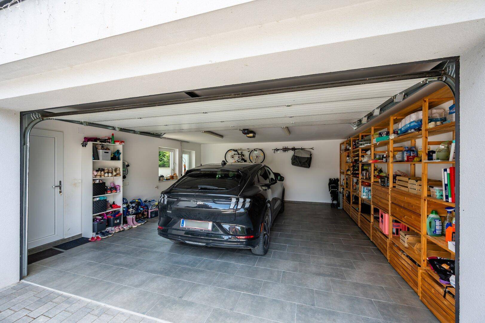 Geräumige Garage mit Fliesenboden, Regalen und Platz für ein Fahrzeug sowie Fahrräder.