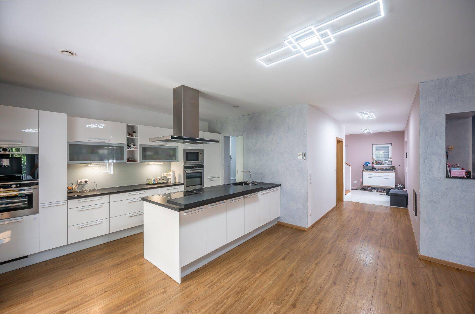 Moderne, offene Küche mit weißen Hochglanzfronten, Kücheninsel und Holzboden.