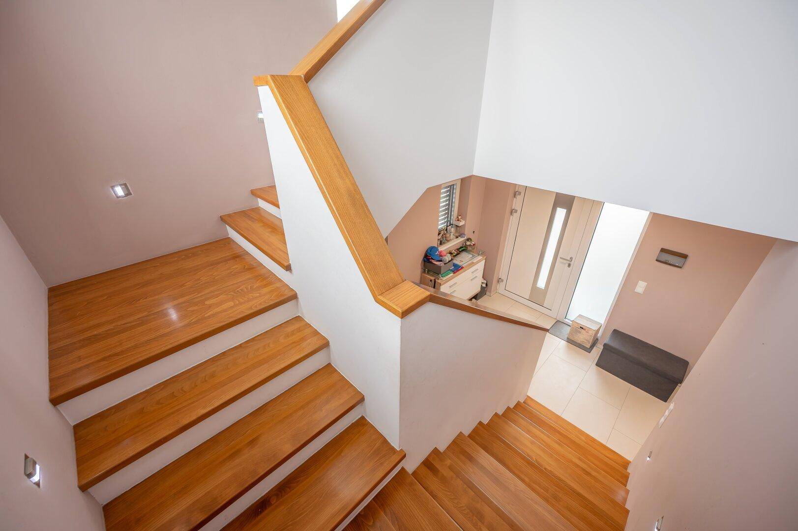 Helle Holztreppe führt in die obere Etage, mit natürlichem Lichteinfall durch ein Fenster.