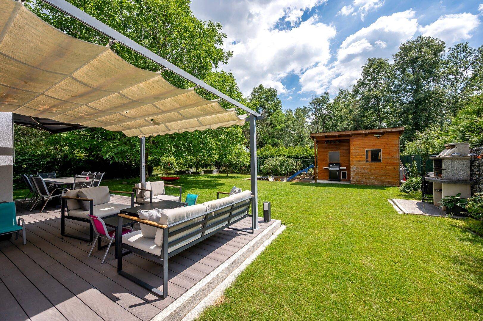 Großer, gepflegter Garten mit einer möblierten Terrasse, Sonnenschutz und einem Gartenhaus.